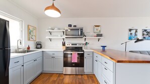 A modern kitchen with light blue cabinets, a stainless steel oven, a microwave, and a wooden countertop. - Big Island Kailua Village 208 1 Bedroom Condo (Kailua-Kona)