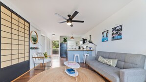 A modern living room with a grey sofa, a round woven rug, and a ceiling fan. - Big Island Kailua Village 208 1 Bedroom Condo (Kailua-Kona)