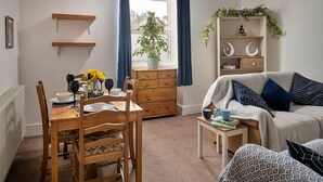 Ein gemütliches Wohnzimmer mit Esstisch, Holzstühlen, einer Couch und einem Bücherregal.