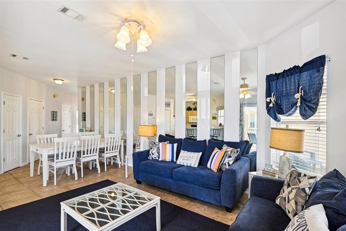 A modern living room with a blue sofa, white chairs, a coffee table, and a dining area.