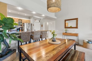 A modern kitchen with wooden cabinets, a stainless steel refrigerator, and a dining area with a wooden table and chairs.