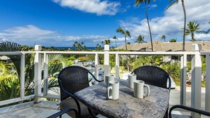 A balcony with a table and chairs, overlooking a coastal area with palm trees and a view of the ocean. - Grand Champions Two Bedrooms - Ocean View by Coldwell Banker Island Vacations (Kihei)