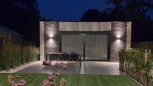 Un patio moderno al aire libre con un muro de piedra, una puerta corrediza de vidrio y una mesa de comedor con sillas.
