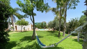 Eine Hängematte in einem üppigen, grünen Garten mit Pool und einer Sitzgelegenheit im Hintergrund.