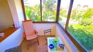 Ein kleiner Balkon mit einem Holzstuhl, einem Tisch mit grüner Tischdecke und Blick auf Garten und Gebäude.