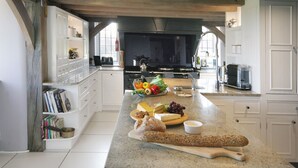 Una cocina con armarios blancos, encimera de mármol y diversos alimentos, incluyendo pan, queso y verduras.