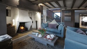Una sala de estar acogedora con chimenea, un sofá azul, una mesa de centro con juego de té y una escalera que sube a otro nivel.