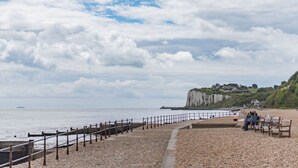 A pebbled beach with a wooden fence, benches, and a cliff in the background.