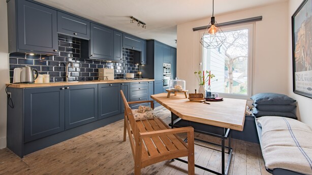 A modern kitchen with dark blue cabinets, a wooden countertop, and a bench.