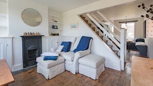 A living room with a fireplace, white sofas, a staircase, and a wooden floor.