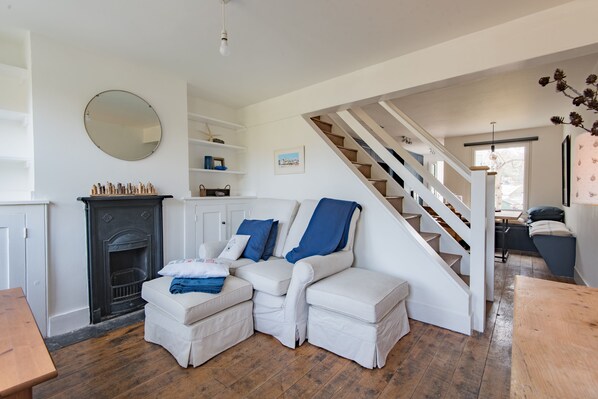 A living room with a fireplace, white sofas, a staircase, and a wooden floor. - Pretty cottage near the sea, Poppy Cottage (Kingsdown)