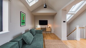 Ein modernes Wohnzimmer mit einem grünen Sofa, Holzboden, einem an der Wand montierten Fernseher und Dachfenstern.