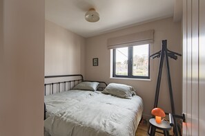Een slaapkamer met een bed, een raam en een hangstoel.