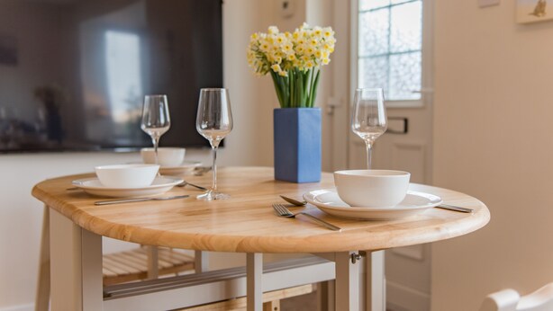 A dining table with white plates, bowls, and cutlery, a vase with yellow flowers, and two wine glasses. - Lovely modern house near the golf course and sea - Links Bay (Deal)