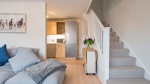 A modern living room with a sofa, a small table with a vase, and a staircase leading to an upper floor. - Lovely modern house near the golf course and sea - Links Bay (Deal)