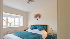 A bedroom with a bed, a window, a nightstand, and a wall-mounted lamp. - Lovely modern house near the golf course and sea - Links Bay (Deal)
