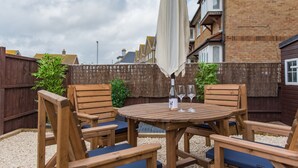 A wooden outdoor seating area with a table and chairs, a bottle, and two glasses. - Lovely modern house near the golf course and sea - Links Bay (Deal)