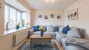 A modern living room with a grey sofa, a wooden coffee table, and a blue rug. - Lovely modern house near the golf course and sea - Links Bay (Deal)