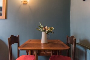 Ein Holztisch mit einer weißen Blumenvase, zwei Holzstühle und einer Wandleuchte.