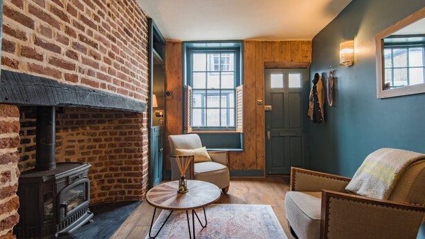 A cozy room with a brick fireplace, a wooden bench, a round table, and a blue wall. - Charming cottage by the sea - Coop's Landing (Deal)