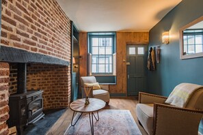 Una habitación acogedora con chimenea de ladrillo, un banco de madera, una mesa redonda y una pared azul.