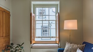 A room with a window, a blue sofa, a lamp, and a plant. - Charming cottage by the sea - Coop's Landing (Deal)