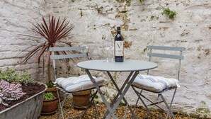 A small outdoor seating area with a table and two chairs, a bottle of wine, and potted plants. - Charming cottage by the sea - Coop's Landing (Deal)