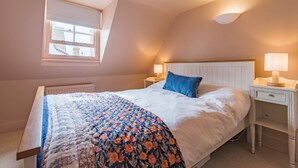 A bedroom with a bed, a nightstand, a lamp, a window, and a radiator. - Charming cottage by the sea - Coop's Landing (Deal)