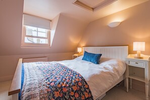 Une chambre à coucher avec un lit, une table de chevet, une lampe, une fenêtre et un radiateur.
