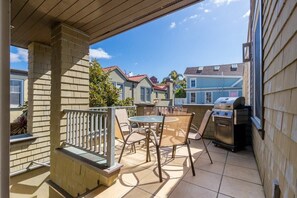 Un patio techado con una parrilla, asientos exteriores y vistas de casas vecinas.