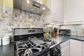 A kitchen with a gas stove, a microwave, and a tiled backsplash. - Capitola Village Retreat with Garage! (Capitola)