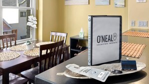 A dining area with a table set for two, a chair, a potted plant, and a framed sign for O'Neal vacation rentals.