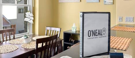 A dining area with a table set for two, a chair, a potted plant, and a framed sign for O'Neal vacation rentals.