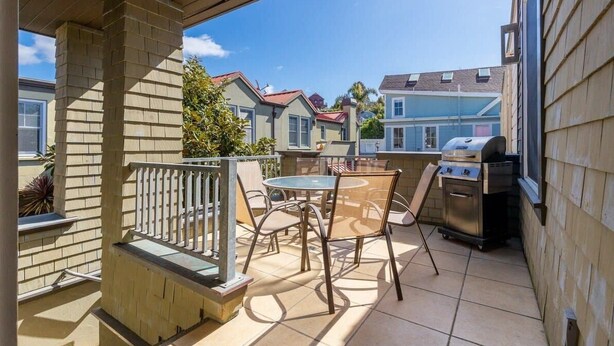 A covered patio with a grill, outdoor seating, and a view of neighboring houses.