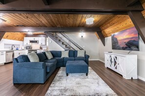 A loft-style living space with a sectional sofa, a white console table, and a large window with a sunset view. - Rustic & Modern 3BDR Tahoe Cabin (Tahoe City)