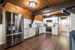 A modern kitchen with stainless steel appliances, wooden ceiling beams, and white cabinetry. - Rustic & Modern 3BDR Tahoe Cabin (Tahoe City)