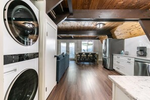 A compact kitchen with a built-in washer and dryer, a dining area with a table and chairs, and a view through a glass door. - Rustic & Modern 3BDR Tahoe Cabin (Tahoe City)