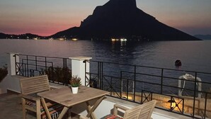 Een terras met zitplaatsen en uitzicht op een berg en een wateroppervlak bij zonsondergang.