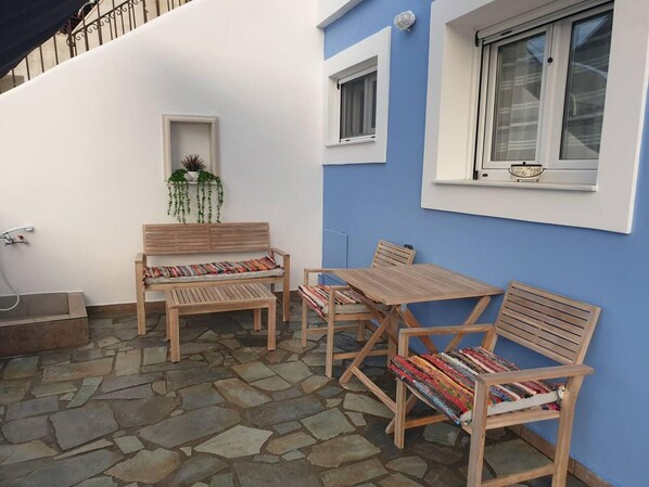 A patio with stone flooring, wooden furniture, and a blue wall with windows.