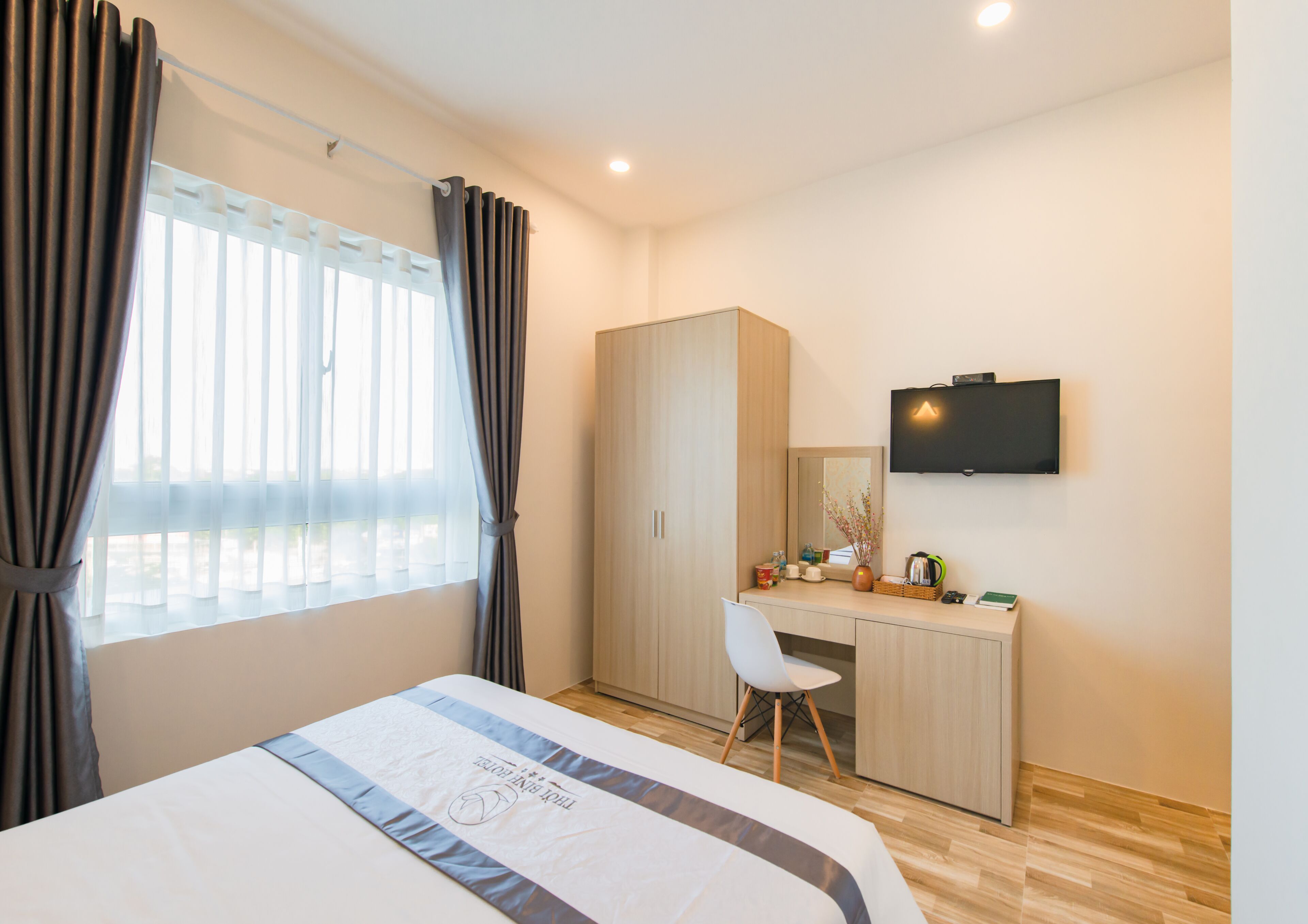 A hotel room with a bed, a desk, a chair, a television, and a wardrobe.