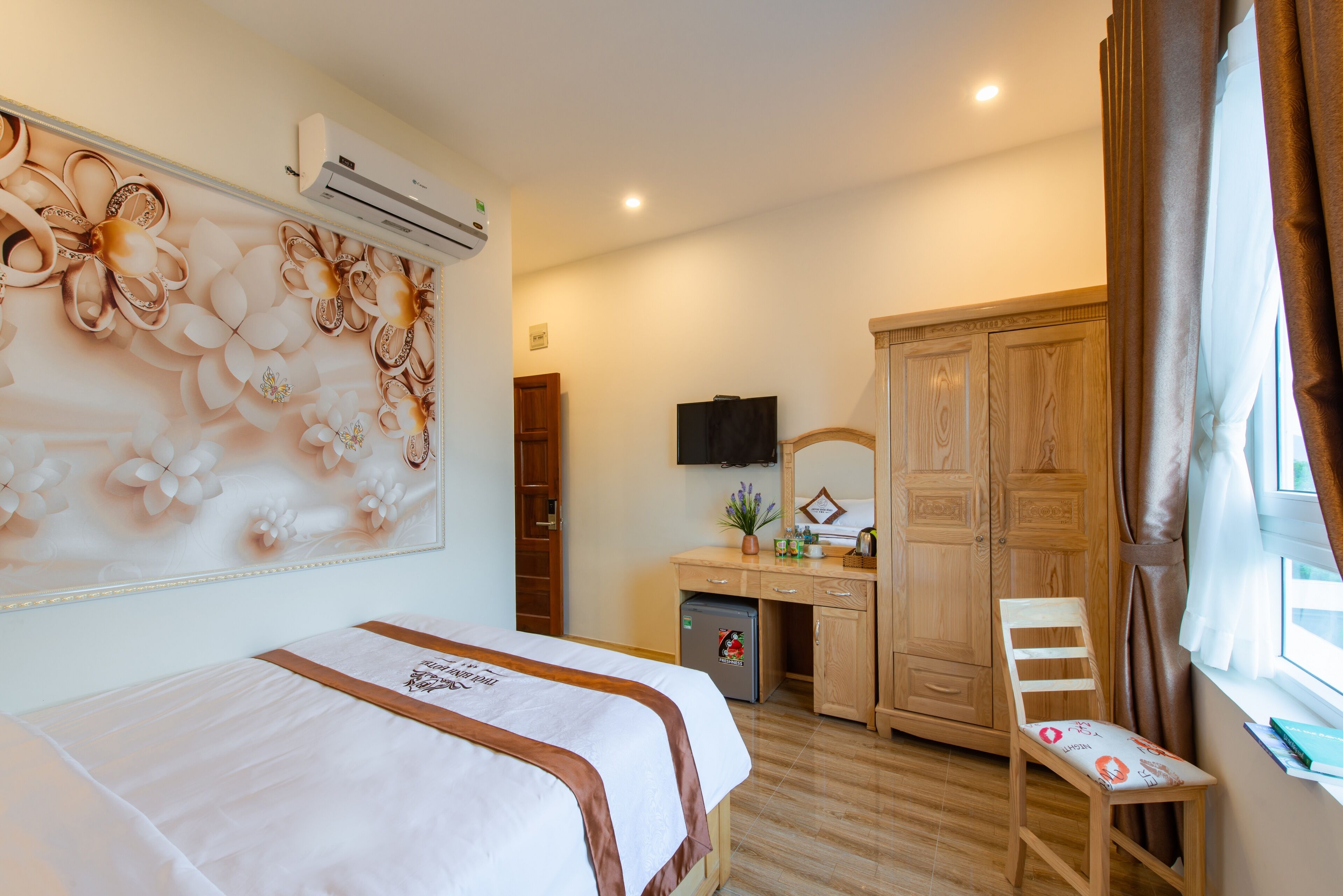 A hotel room with a bed, a desk, a chair, a wardrobe, and an air conditioning unit.