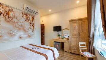 A hotel room with a bed, a desk, a chair, a wardrobe, and an air conditioning unit.
