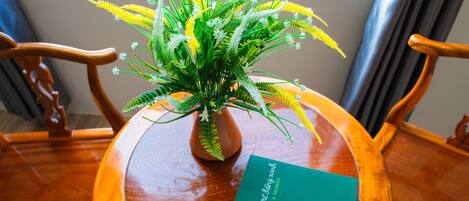 A wooden table with a green book titled "The Big Book of Singing Knots" and a potted plant with yellow and white flowers.