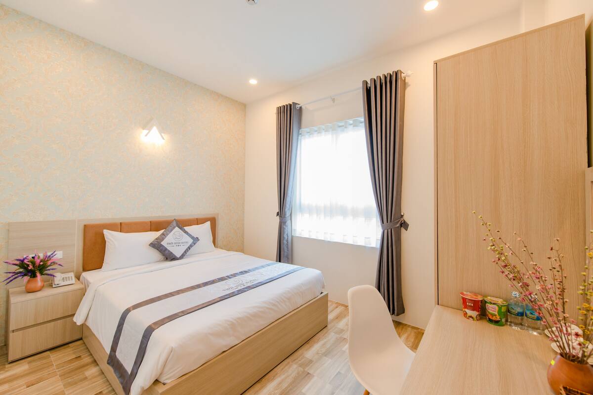 A hotel room with a bed, bedside table, chair, and a window with curtains.