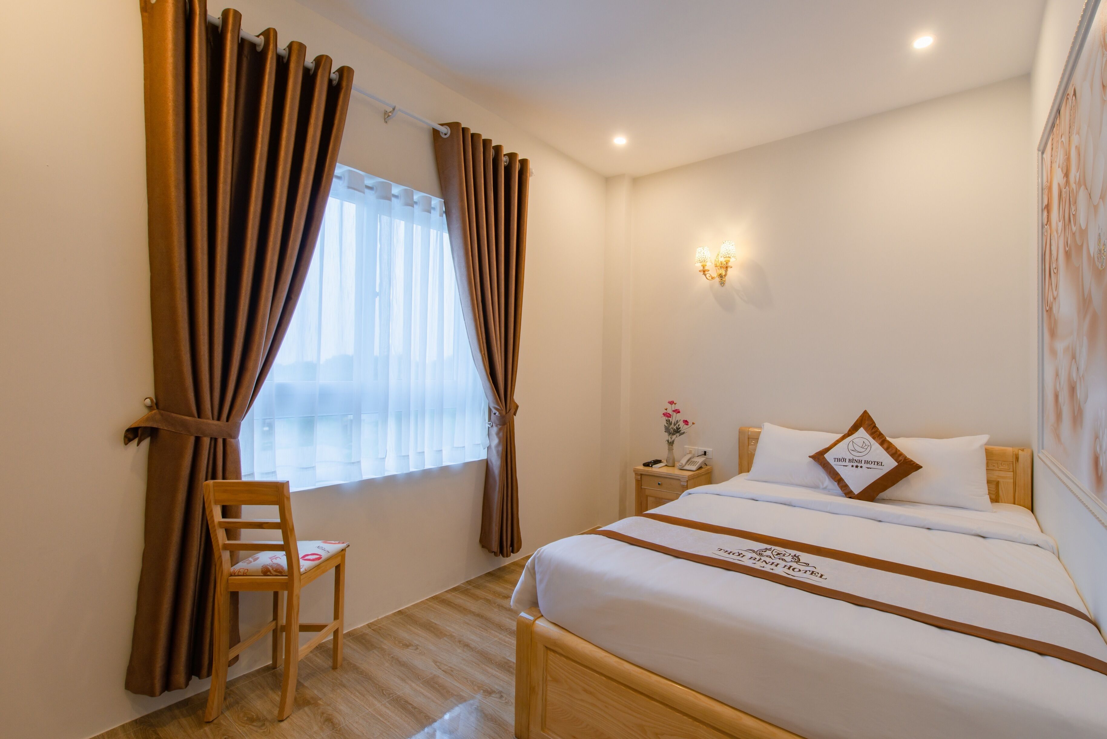 Quarto de hotel com cama, uma cadeira, mesa de cabeceira, luminária e janela com cortinas.