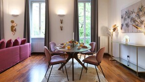 Una sala de estar moderna con una mesa redonda preparada para el desayuno, un sofá rosa y un ventanal con cortinas.