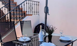 Een gedekte tafel met borden, glazen, een fles en een kleine plant, met een trap en balustrade op de achtergrond.