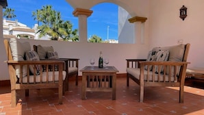 A terrace with two wooden sofas, a small table, and a bottle of wine. - South facing Los Dolses bungalow - comm pool LD186 (Los Dolses)