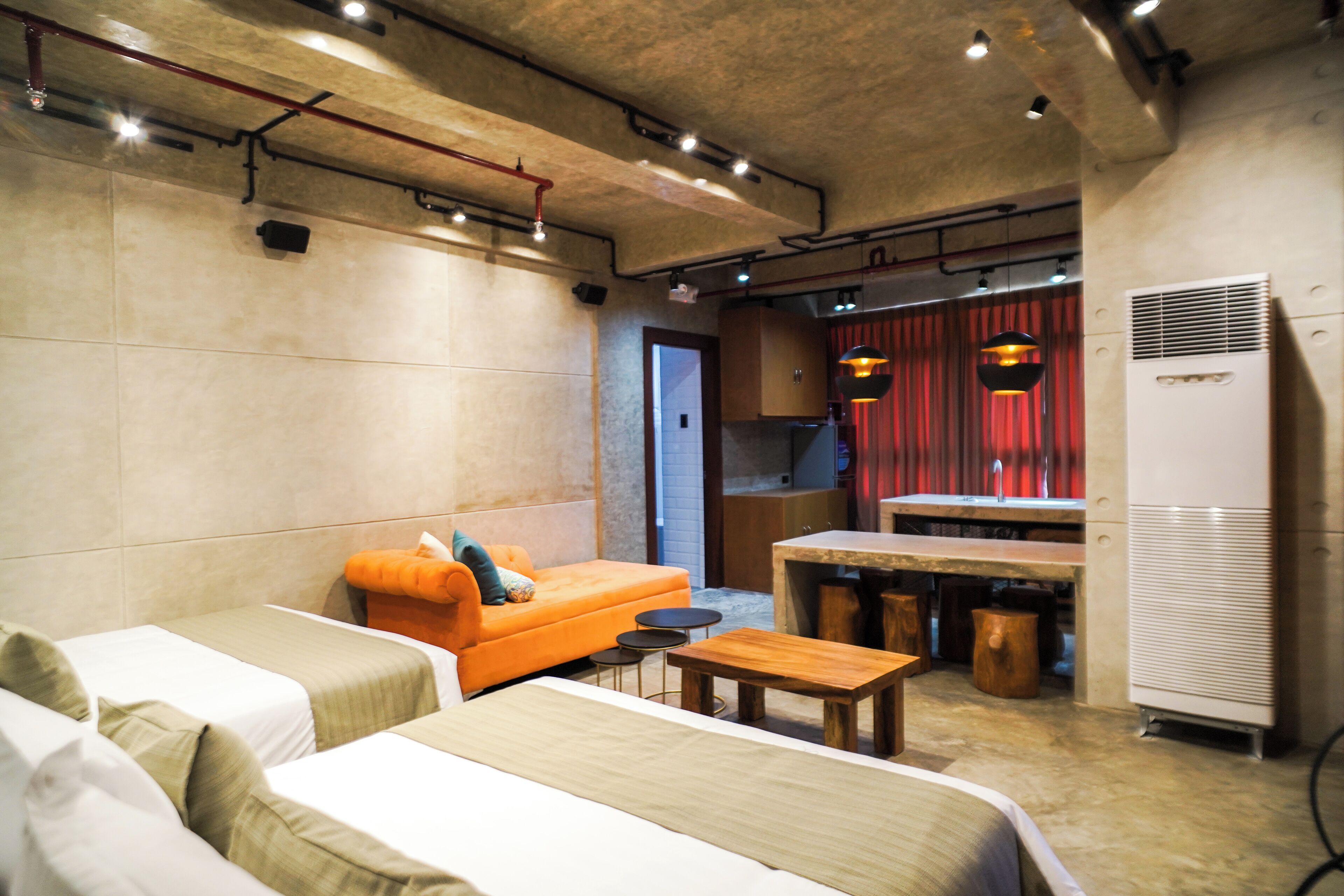 A modern hotel room with a sofa, two beds, a dining table, and a kitchen area.