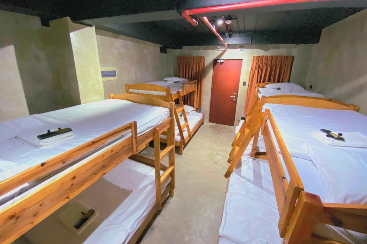 A dormitory room with bunk beds, a red door, and a ceiling light fixture.